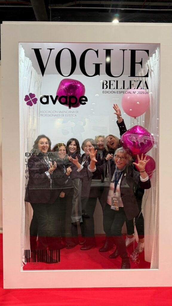 Socias de AVAPE posando tras el photocall con forma de portada de Vogue Belleza, con globos magenta, en el stand de la asociación